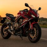 夕焼けに照らされるホンダ CBR650R が郊外の道路に停車しているシーン。赤と黒のボディが夕日を反射し、高品質な16:9構図でバイクの美しいデザインと質感を際立たせたアイキャッチ用画像。