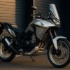 夕方の柔らかな光に照らされたホンダ XL750 トランザルプが、ディーラー前の舗装路に停められている。シルバーの車体が美しく輝き、アドベンチャーバイクとしての存在感と上質さを強調している。