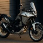 夕方の柔らかな光に照らされたホンダ XL750 トランザルプが、ディーラー前の舗装路に停められている。シルバーの車体が美しく輝き、アドベンチャーバイクとしての存在感と上質さを強調している。